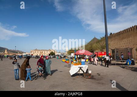 Traditionally dressed women with children, stall with oranges and children playing on carousel and  trampoline on Place Boujloud in Fes (Fez), Morocco Stock Photo
