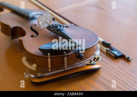 violin lying on a wooden textured table. Violin body and bow on wood table with golden glow. Top view. Horizontal composition. Stock Photo