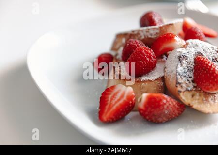 French toast with strawberries and raspberries, sprinkled with powdered sugar. Dessert on a white plate. Stock Photo