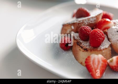 French toast with strawberries and raspberries, sprinkled with powdered sugar. Dessert on a white plate. Stock Photo