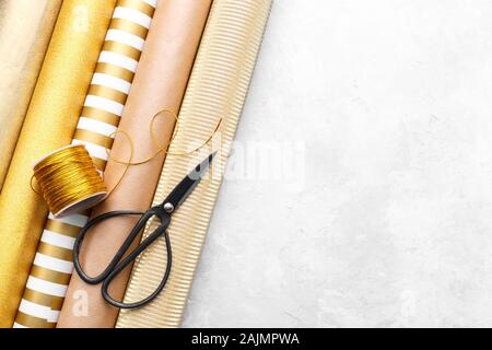 Golden glossy wrapping paper rolls for gift boxes,scissors and ribbon for hobby and crafts on grey stone background, close up with copy space Stock Photo