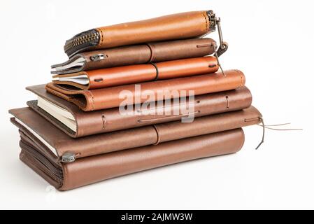 A stack of leather-bound journals, notebooks, cases, and wallets set on a plain white background. Stock Photo