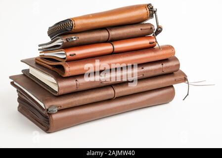 A stack of leather-bound journals, notebooks, cases, and wallets set on a plain white background. Stock Photo