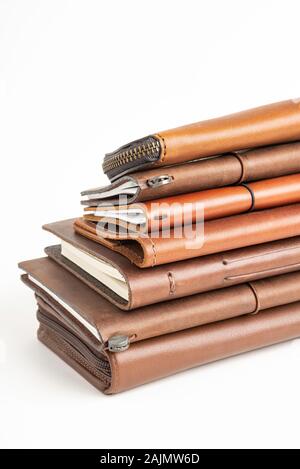 A stack of leather-bound journals, notebooks, cases, and wallets set on a plain white background. Stock Photo
