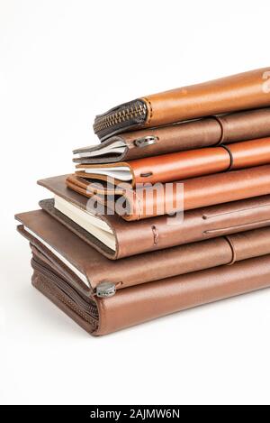 A stack of leather-bound journals, notebooks, cases, and wallets set on a plain white background. Stock Photo