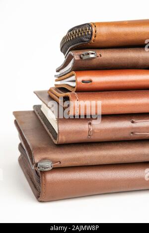 A stack of leather-bound journals, notebooks, cases, and wallets set on a plain white background. Stock Photo