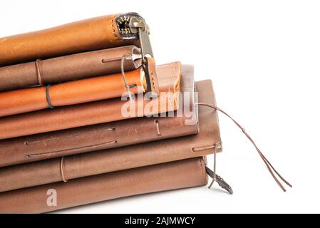 A stack of leather-bound journals, notebooks, cases, and wallets set on a plain white background. Stock Photo