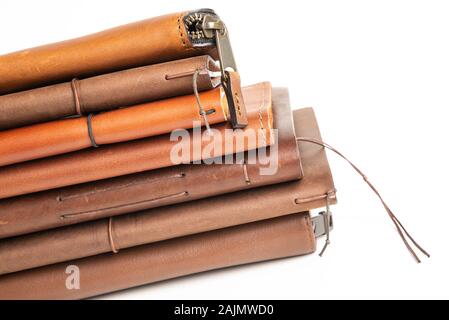 A stack of leather-bound journals, notebooks, cases, and wallets set on a plain white background. Stock Photo