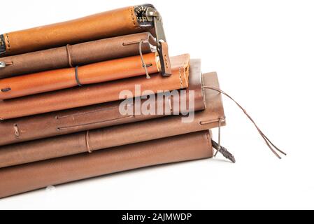 A stack of leather-bound journals, notebooks, cases, and wallets set on a plain white background. Stock Photo