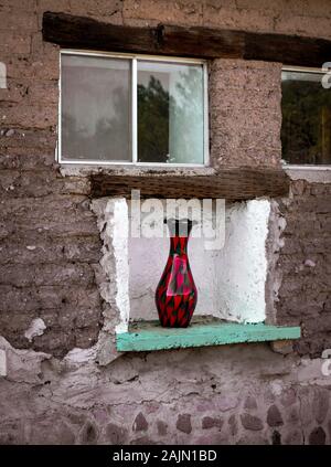A curious site to see a contemporary red and black glass art vase sitting in an outdoor wall niche on an old vintage adobe brick building in Tubac AZ Stock Photo