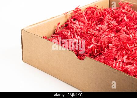 A brown cardboard package box filled with cut and crimped red paper strips set on a plain white background. Stock Photo