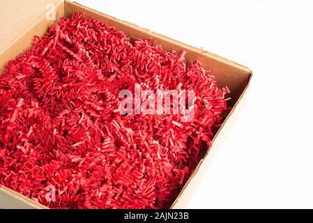 A brown cardboard package box filled with cut and crimped red paper strips set on a plain white background. Stock Photo