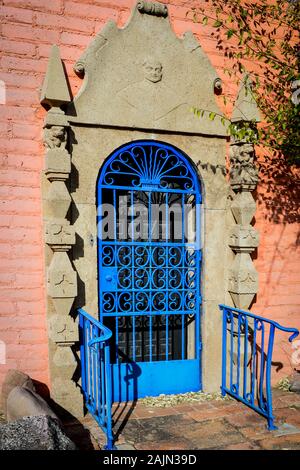 A decorative blue iron gate to entrance with stone carved pillars and a Saint figure in bas relief overhead the door to a rectory in an atmospheric sc Stock Photo