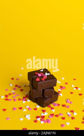 a stack of chocolates on a background of confetti from small hearts. yellow background. Stock Photo