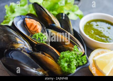 Cooked Mussels with herbs lemon and dark plate background / Fresh seafood shellfish on bowl and spicy sauce in the restaurant mussel shell food Stock Photo