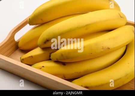 A bunch of ripe yellow bananas on a wooden tray on a white background. Close up Stock Photo