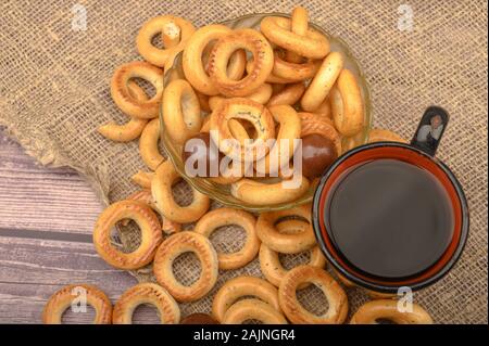 Small bagels, chocolates, a mug of tea and a rough homespun cloth on a wooden background close-up Stock Photo