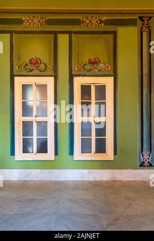 Two narrow closed windows and beautiful elegant carved frames on green wall with ornate border and white marble tiled floor, in abandoned building Stock Photo