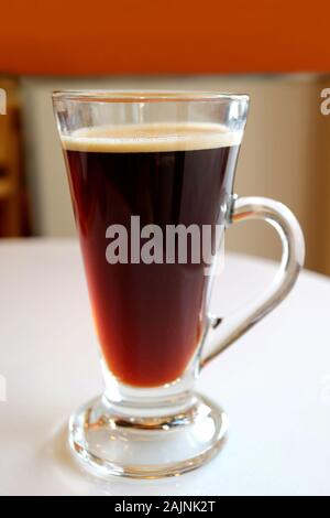 Hot black coffee in a transparent glass served on white table Stock Photo