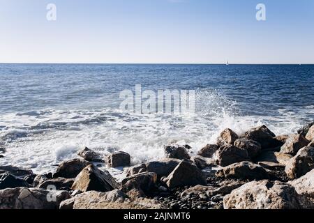 A white crested wave crashes on black lava rocks Stock Photo