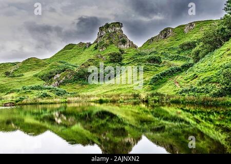 Rocks covered with grass with a reflection of it in a river Stock Photo