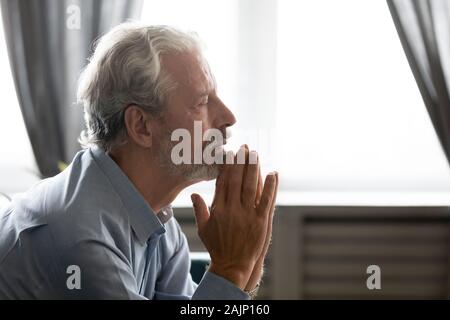50s man closed eyes folding hands in gesture of praying Stock Photo