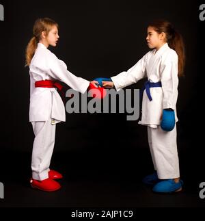 Two little karate women in white kimonos, one in red and the other in blue competition equipment shake hands as a sign of respect before the fight aga Stock Photo