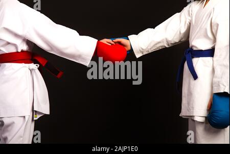 Two little karate women in white kimonos, one in red and the other in blue competition equipment shake hands as a sign of respect before the fight aga Stock Photo