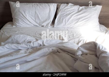 White pillow and blanket on bed unmade. Messy bed after used . wrinkled white bed, pillow and bedsheets Stock Photo
