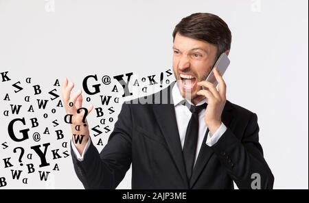 Phone Rage. Furious Businessman Shouting While Talking On Cellphone, Diverse Alphabet Letters Coming Out Of His Mouth, Light Studio Background Stock Photo