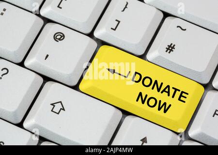 A keyboard with Donate Now written in black lettering on a yellow enter key. Online charity giving money donation concept. England, UK, Britain Stock Photo