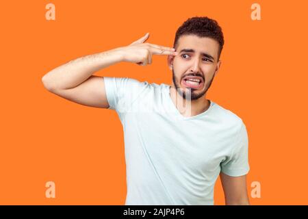 Headshot, kill me please. Portrait of depressed brunette man with beard in white t-shirt committing suicide with finger gun gesture, desperate face ex Stock Photo