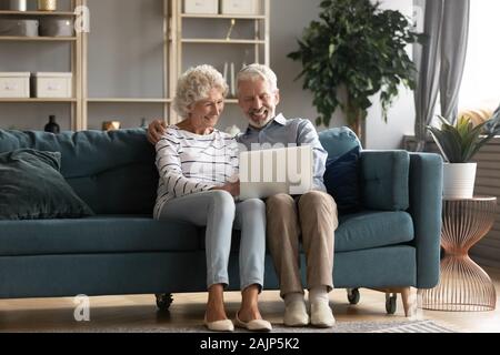 Elderly couple resting on couch using laptop watching movie Stock Photo