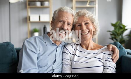 Headshot portrait happy cheerful 60s couple hugging sitting on couch Stock Photo