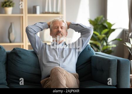 Mature man falls asleep leaned on couch in living room Stock Photo