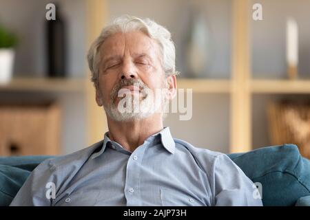 Elderly man closed eyes leaned on sofa having day nap Stock Photo