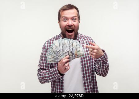 Portrait of amazed satisfied bearded man in casual plaid shirt pointing at dollar banknotes, pleasantly surprised with lottery win, bonus to salary. i
