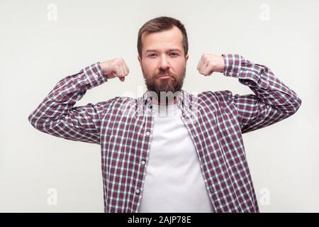 Look at my strength. Portrait of proud bearded man in casual plaid shirt demonstrating biceps on raised hands, feeling power and confidence in victory Stock Photo