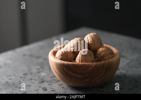 inshell walnuts in olive wood bowl on terrazzo countertop, shallow focus Stock Photo