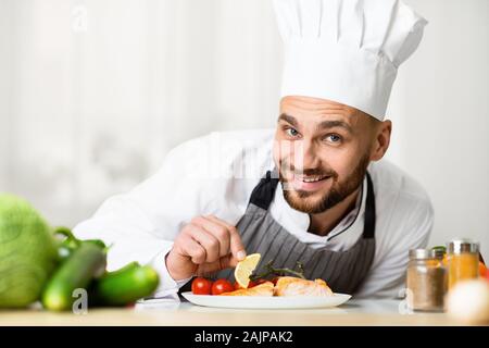 Chef Man Cooking Roasted Salmon Steak Plating Fish Dish Smiling At Camera Standing In Restaurant Kitchen. Selective Focus Stock Photo