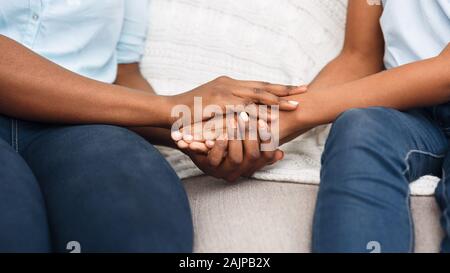 Close Up Black Woman And Child Sitting On Couch Holding Hands, Saying Sorry, Apologize Stock Photo