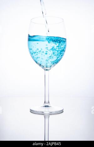 Blue cocktail is poured into a glass on a white background with reflection, splashes and bubbles Stock Photo