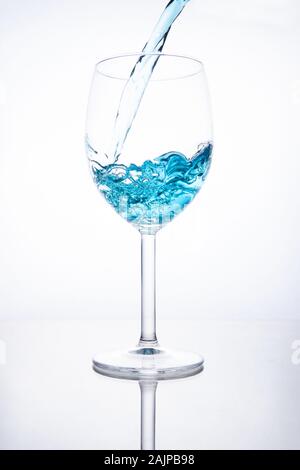 Blue cocktail is poured into a glass on a white background with reflection, splashes and bubbles Stock Photo