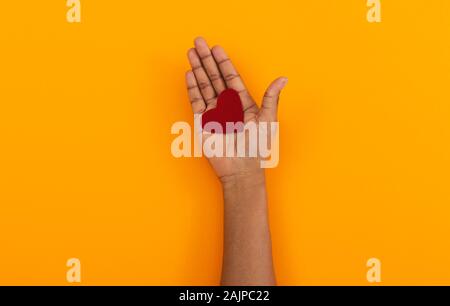 Valentines Day Concept. Red felt heart in opened palm of african american woman over orange studio background, copy space Stock Photo