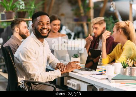 Male designer using laptop and looking at camera with team working on background Stock Photo