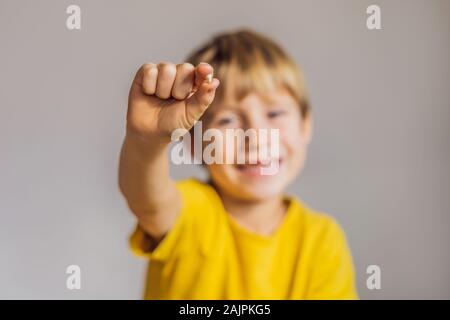 Litle caucasian boy holds a dropped milk tooth between his fingers and laughs looking into the camera Stock Photo