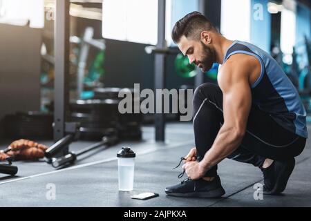 Fitness workout. Young athlete tying sneakers laces at gym, empty space Stock Photo