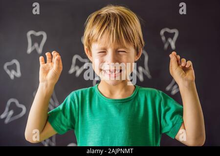 Litle caucasian boy holds a dropped milk tooth between his fingers and laughs looking into the camera Stock Photo