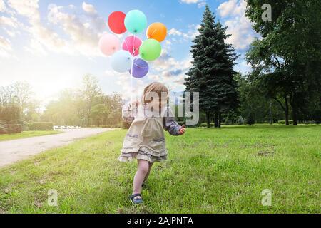 Little girl in a park playing on a grass. Cute little girl in a park. Little Lady with a ballons Stock Photo