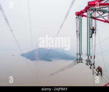 (200105) -- BEIJING, Jan. 5, 2020 (Xinhua) -- Aerial photo taken on Jan. 3, 2019 shows staff members working on the cables between two 380-meter-tall power supply pylons in Zhoushan, east China's Zhejiang Province, (Xinhua/Xu Yu) Stock Photo